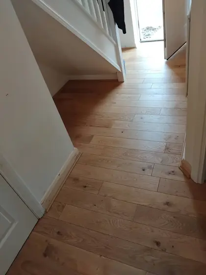 Natural oak plank flooring running through a hallway and under the stairs